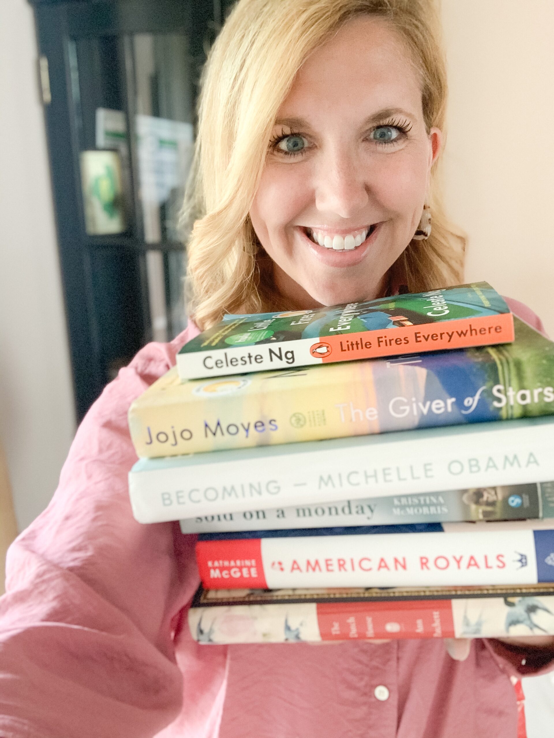 blonde woman with stack of popular books for book-a-month reading challenge