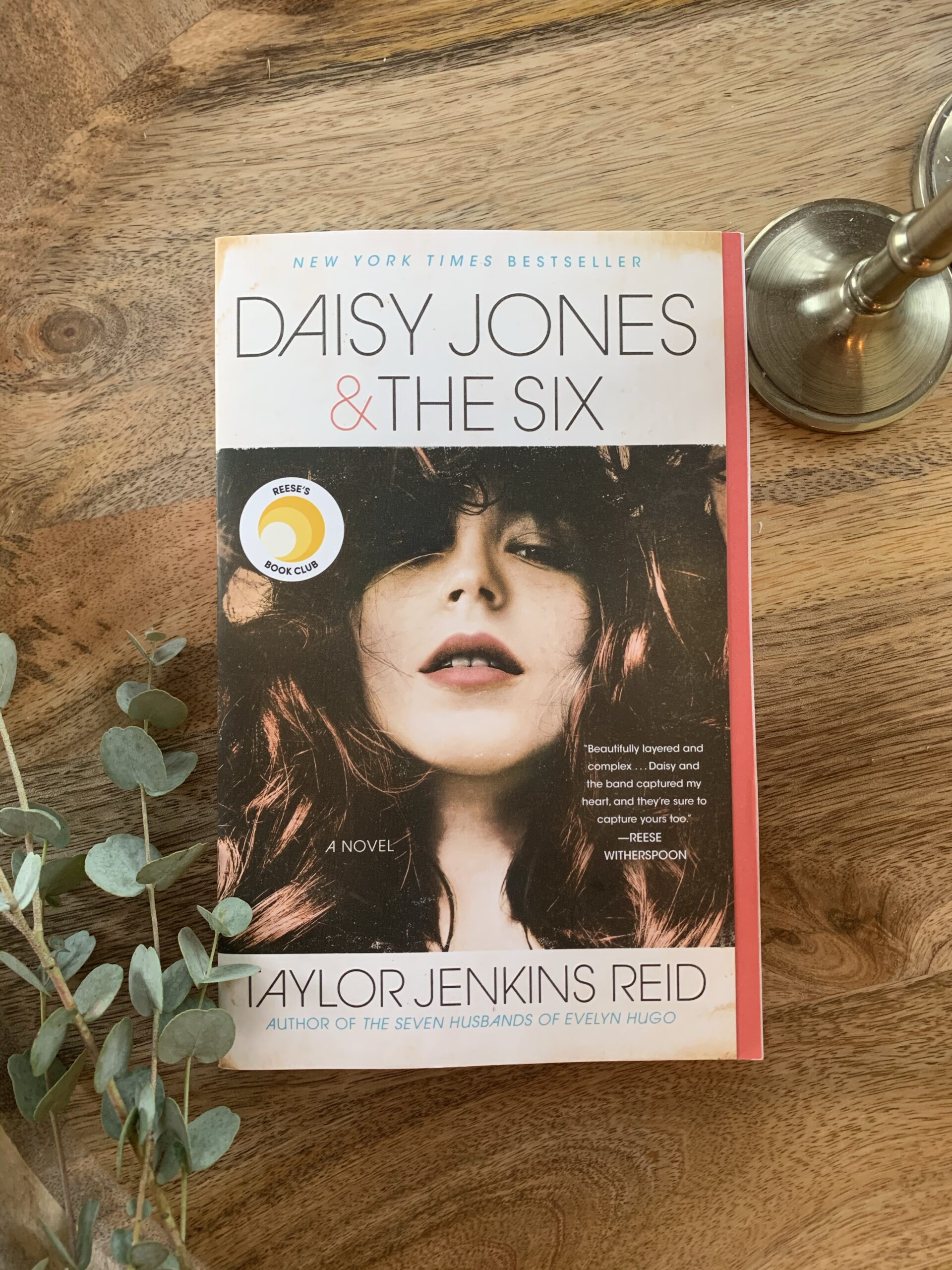 Image of the novel Daisy Jones and the Six, a novel by Taylor Jenkins Reid. Book with image of rock star sits on a wooden tray.