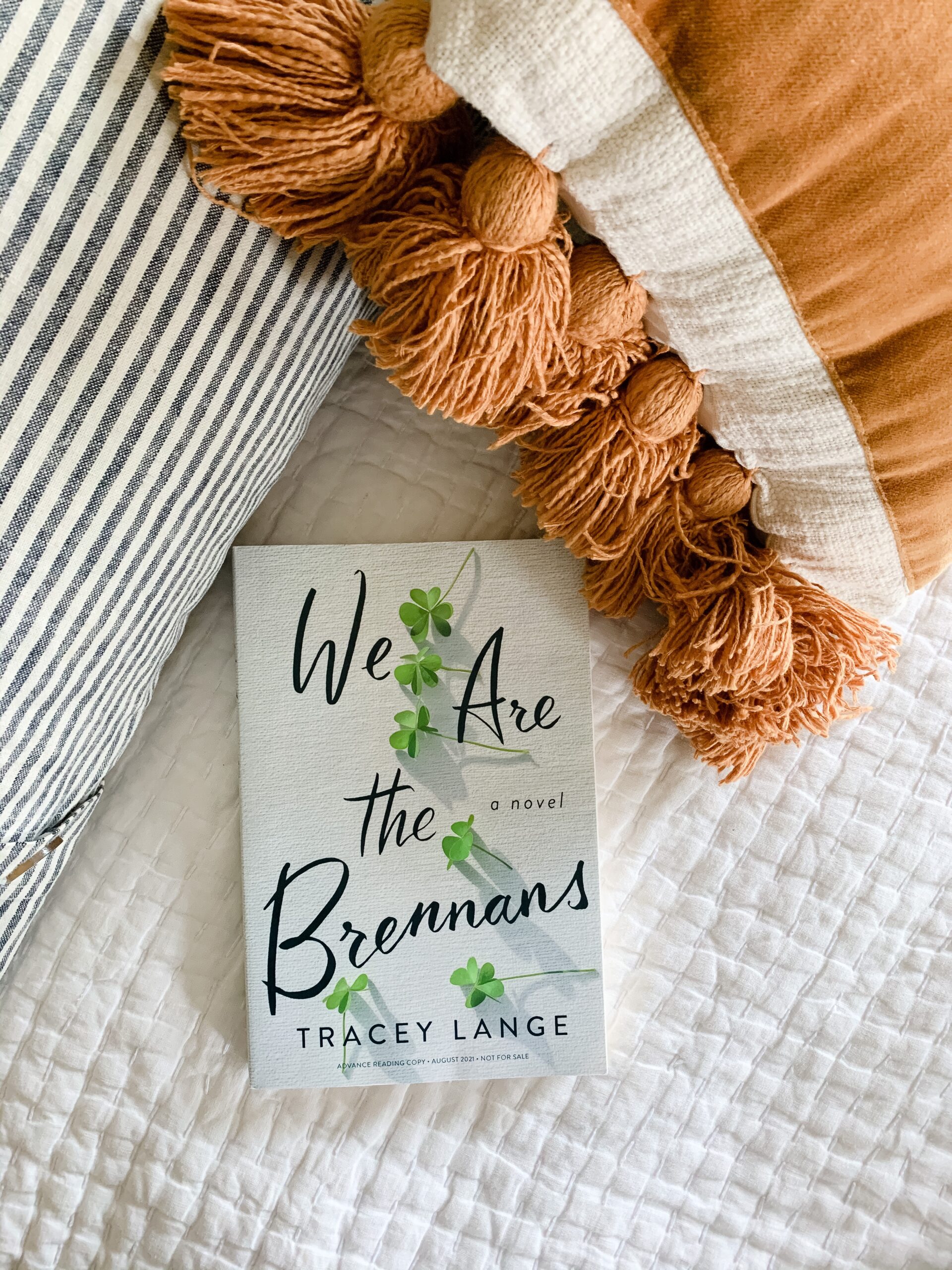 Image of We Are the Brennans novel by Tracey Lange on a bed surrounded by pillows.